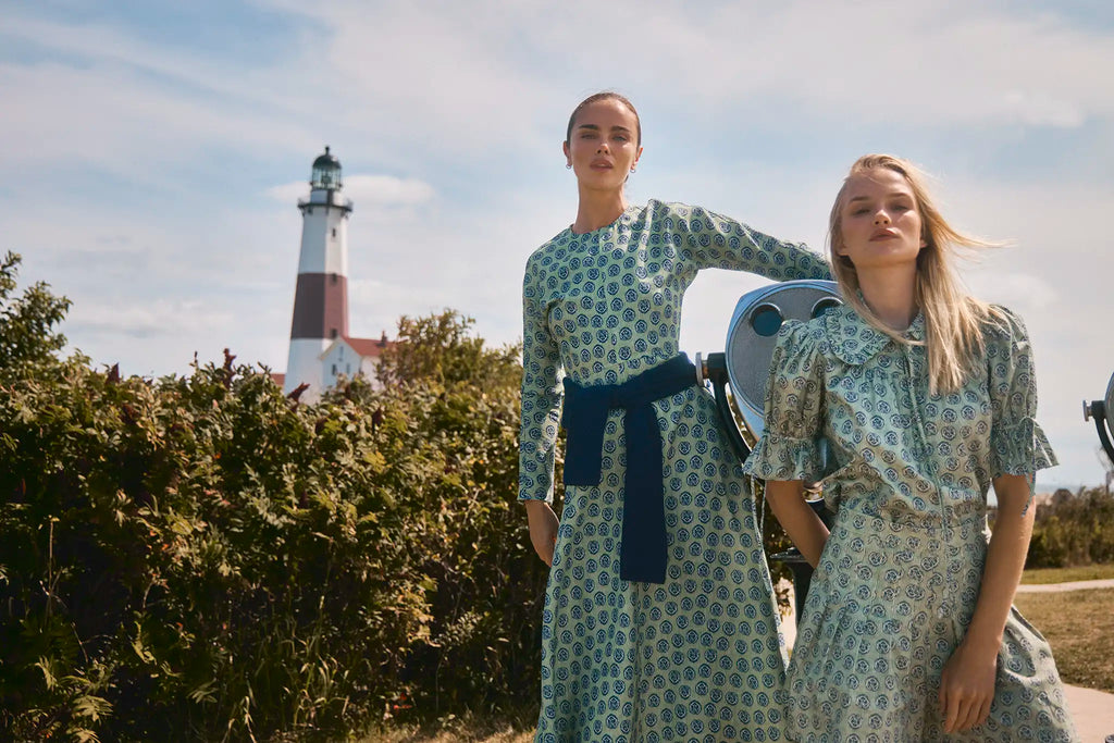Two girls - one in a green longsleeve dress with navy accents other girl in same print but matching top and short in front of lighthouse