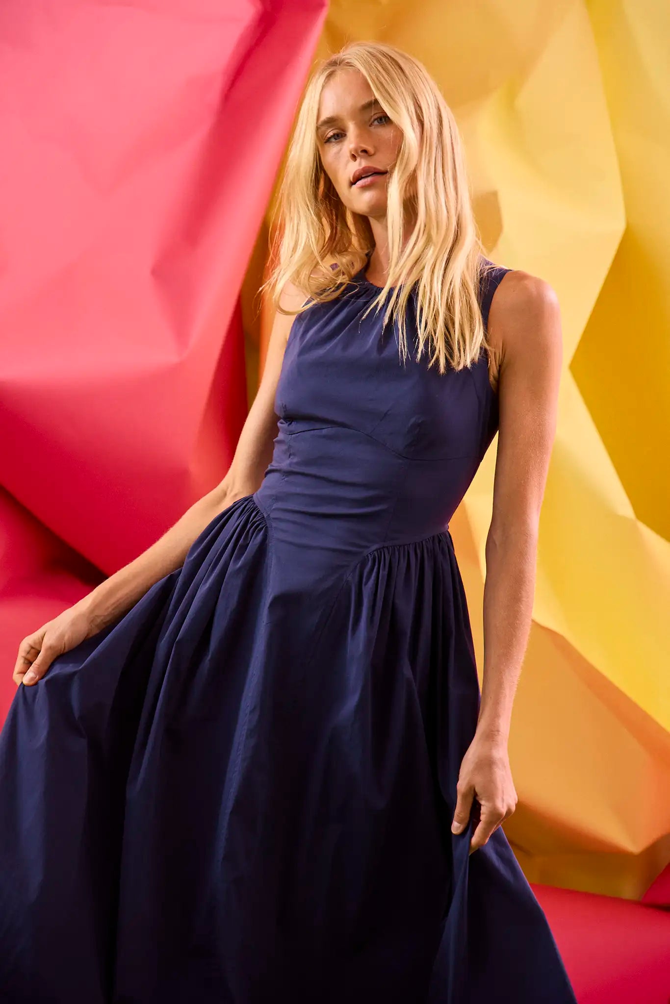 A sleeveless midi navy dress with a fitted bustier bodice, crew neckline, and a bustled full skirt.